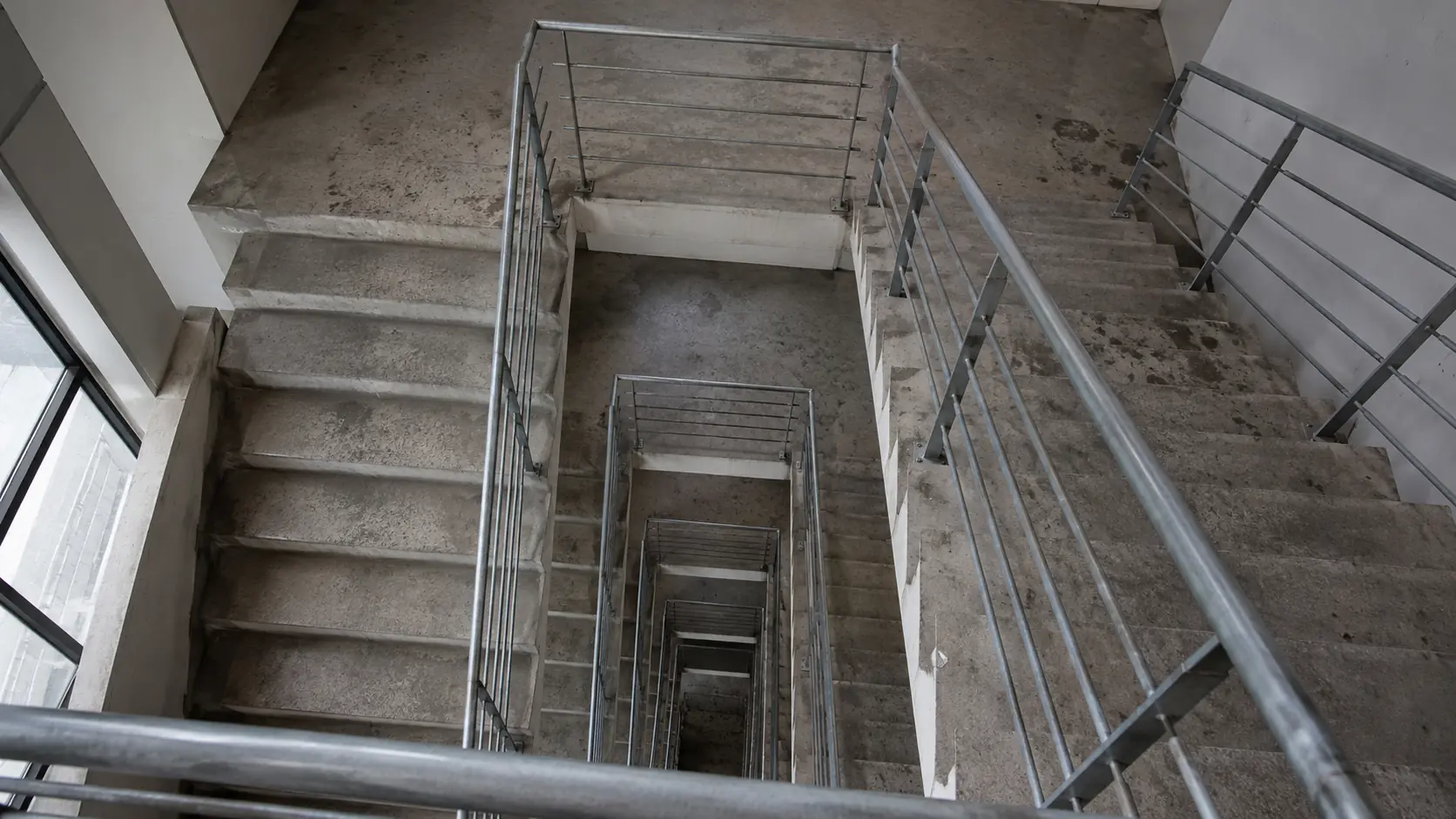Vue plongeante dans une cage d’escalier industrielle, plusieurs volées et rampe métallique